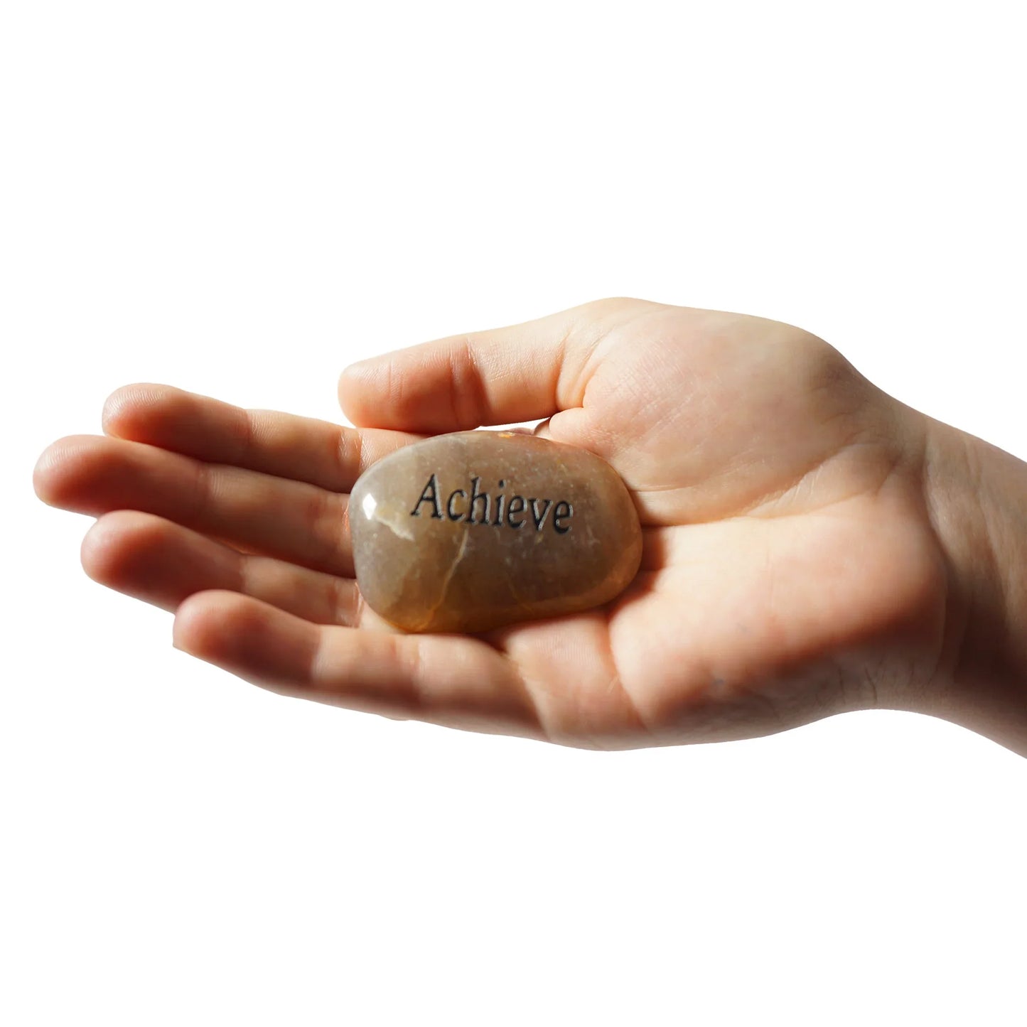 Hand holding a stone with 'Achieve' engraved on it against a white background