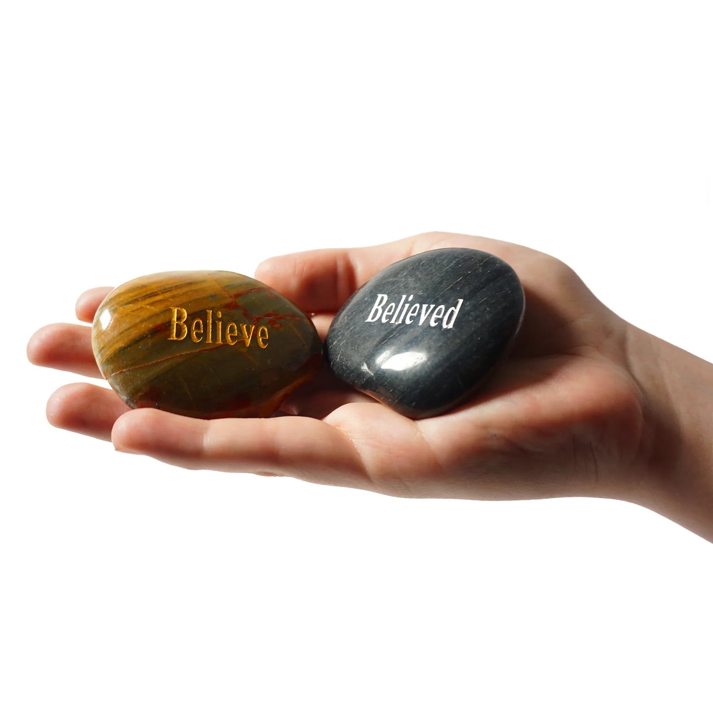 Hand holding two stones, one engraved 'Believe' and the other 'Believed', on a white background.