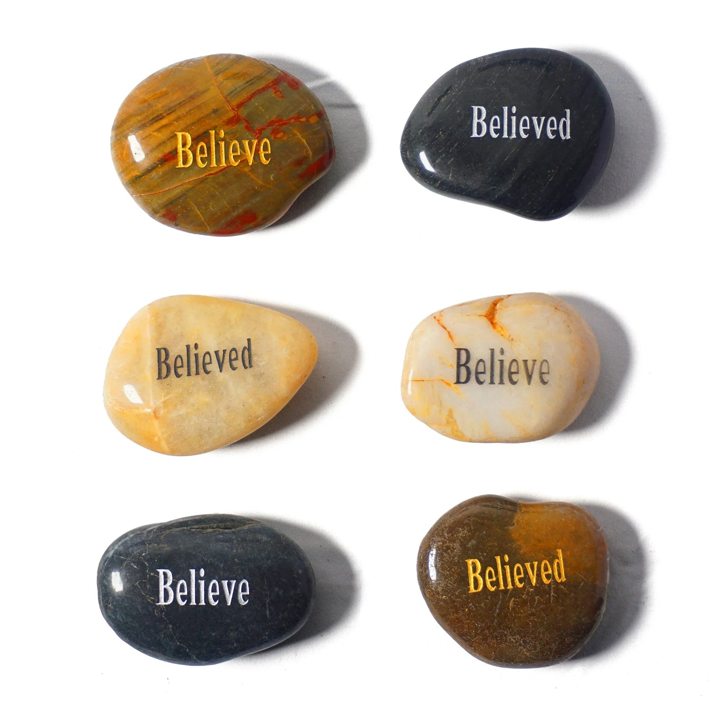 Set of six stones with 'Believed' engraved on them, on a white background