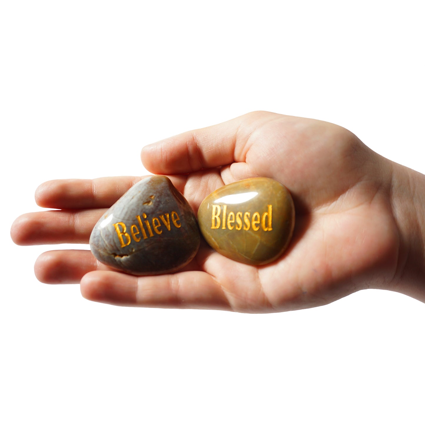Hand holding two stones with 'Believe' and 'Blessed' inscriptions on a white background