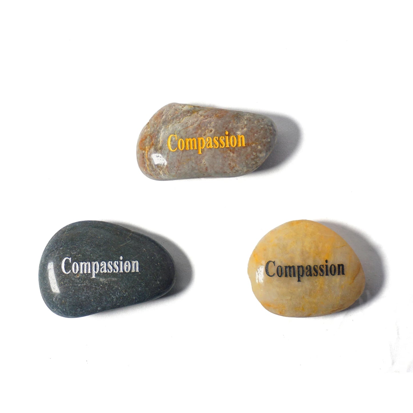 Three stones with the word 'Compassion' engraved on them, each in different colors.