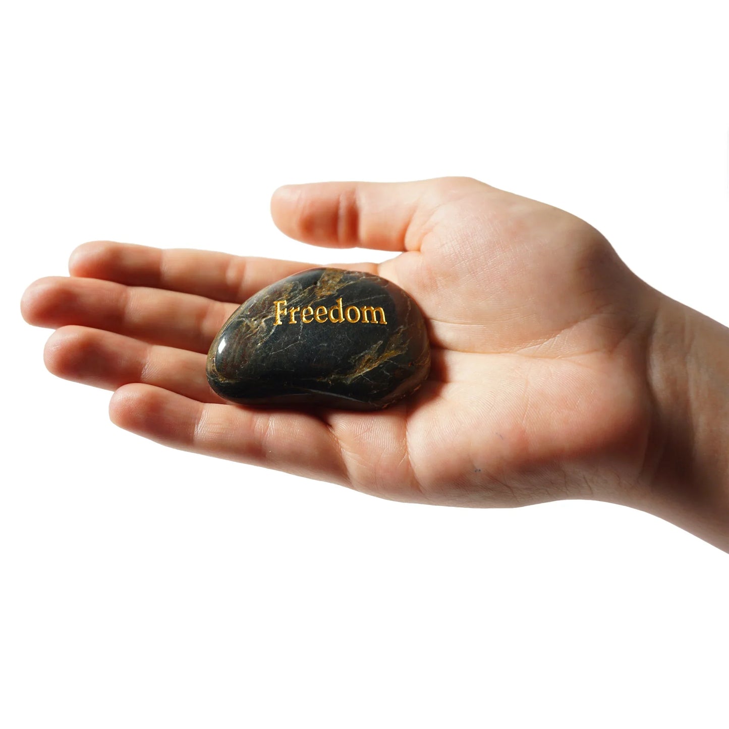 Hand holding a black stone with 'Freedom' engraved on it against a white background