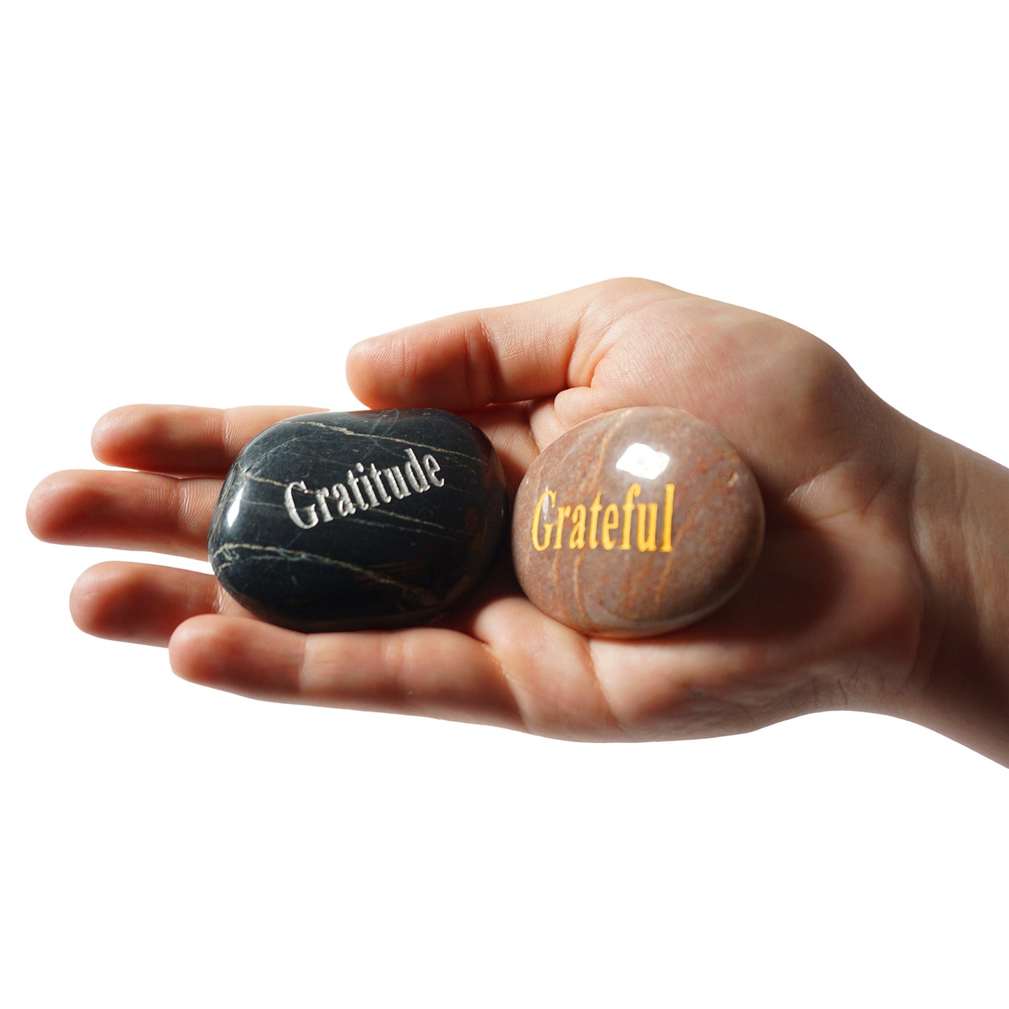 Hand holding two stones with 'Gratitude' and 'Grateful' inscriptions on a white background