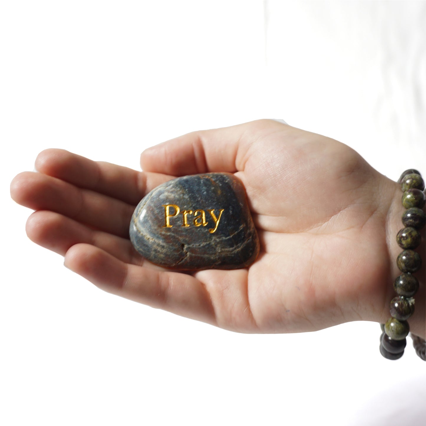 Hand holding a stone with 'Pray' engraved on it against a white background