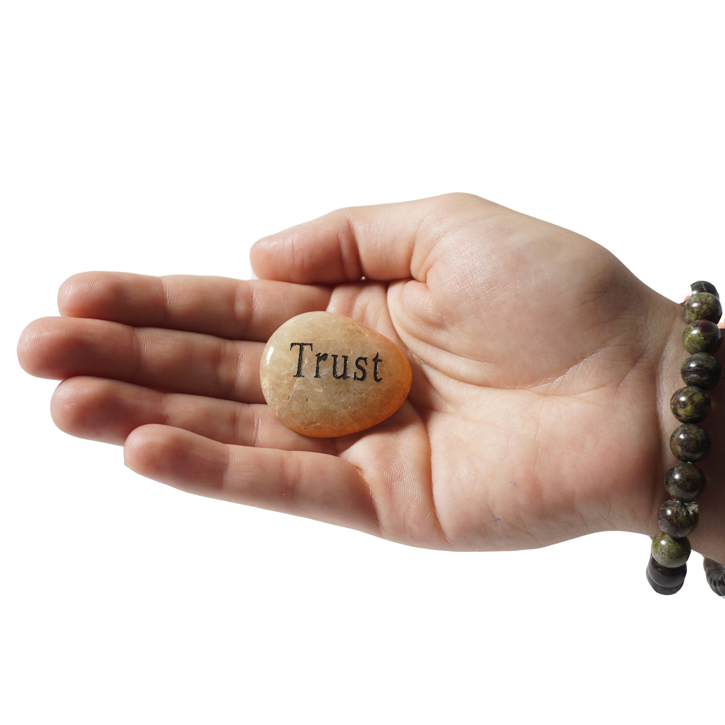 Hand holding a stone with 'Trust' engraved on it against a white background