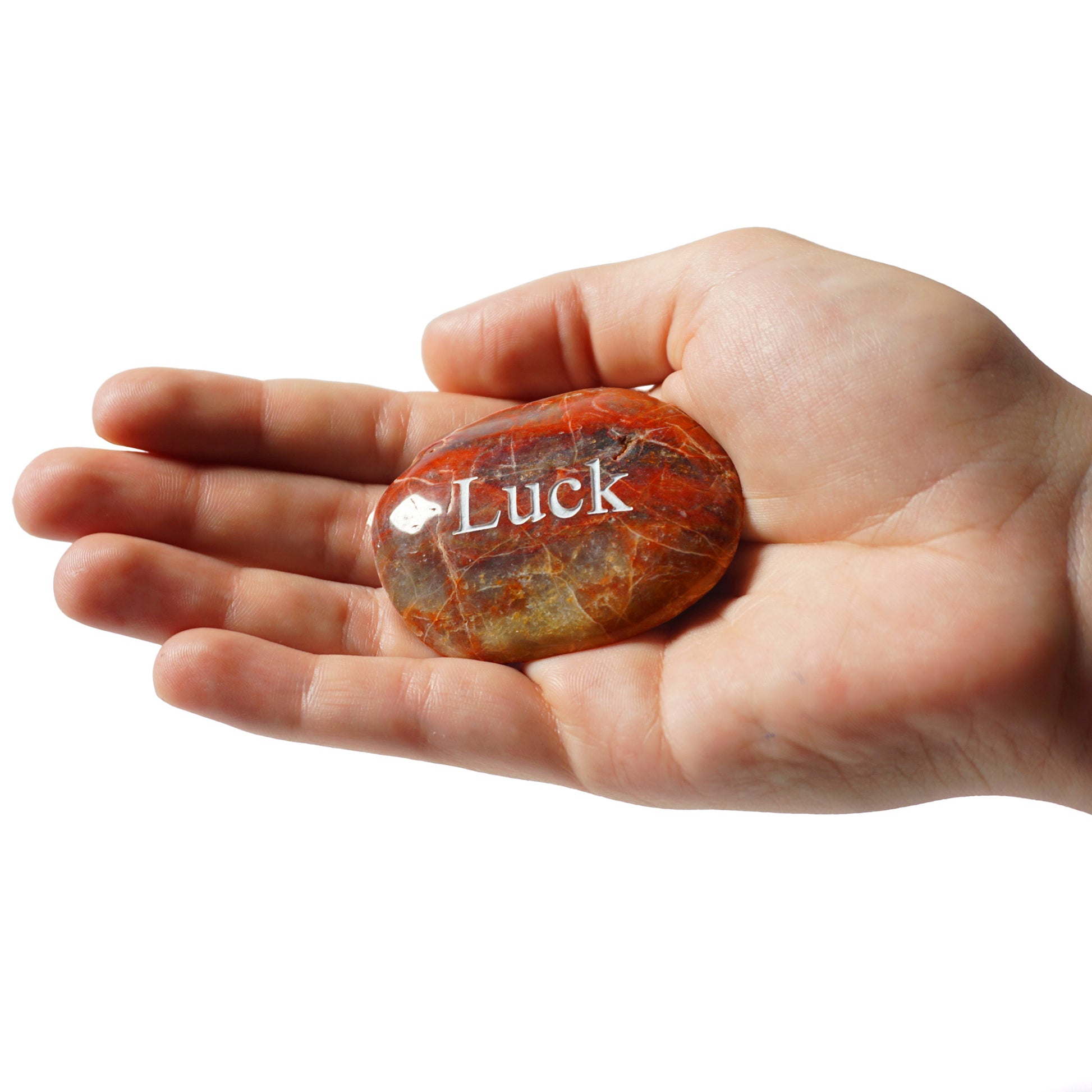 Hand holding a red jasper stone with 'Luck' engraved on it against a white background